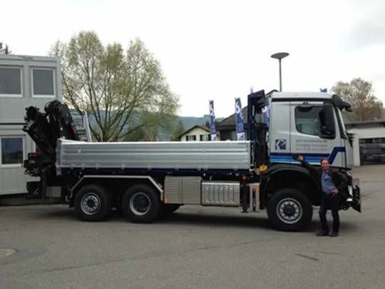 Ein weisser Pritschenwagen parkt im Freien; daneben steht eine Person.