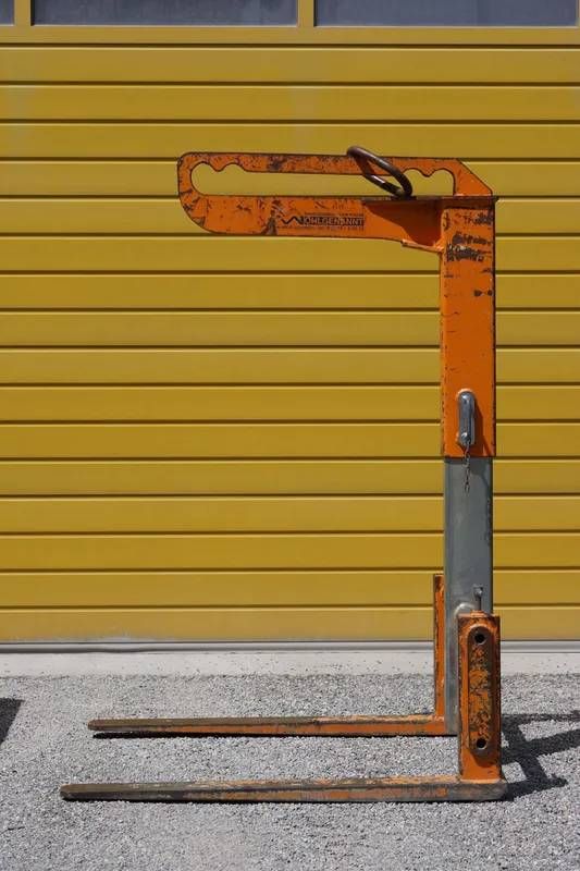 Oranger Handhubwagen vor einer gelben Wand auf Betonboden.