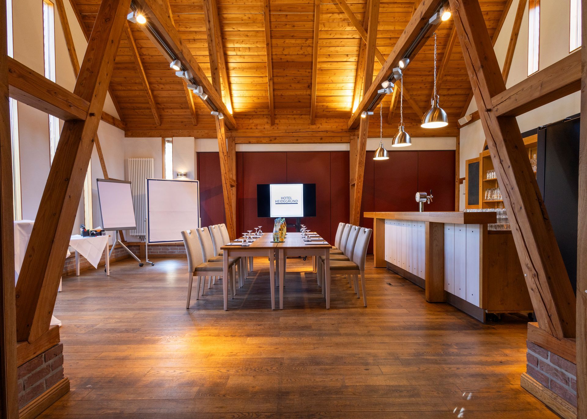 A rustic meeting room with exposed wooden beams, a central conference table, chairs, and a bar counter set against a deep red wall.