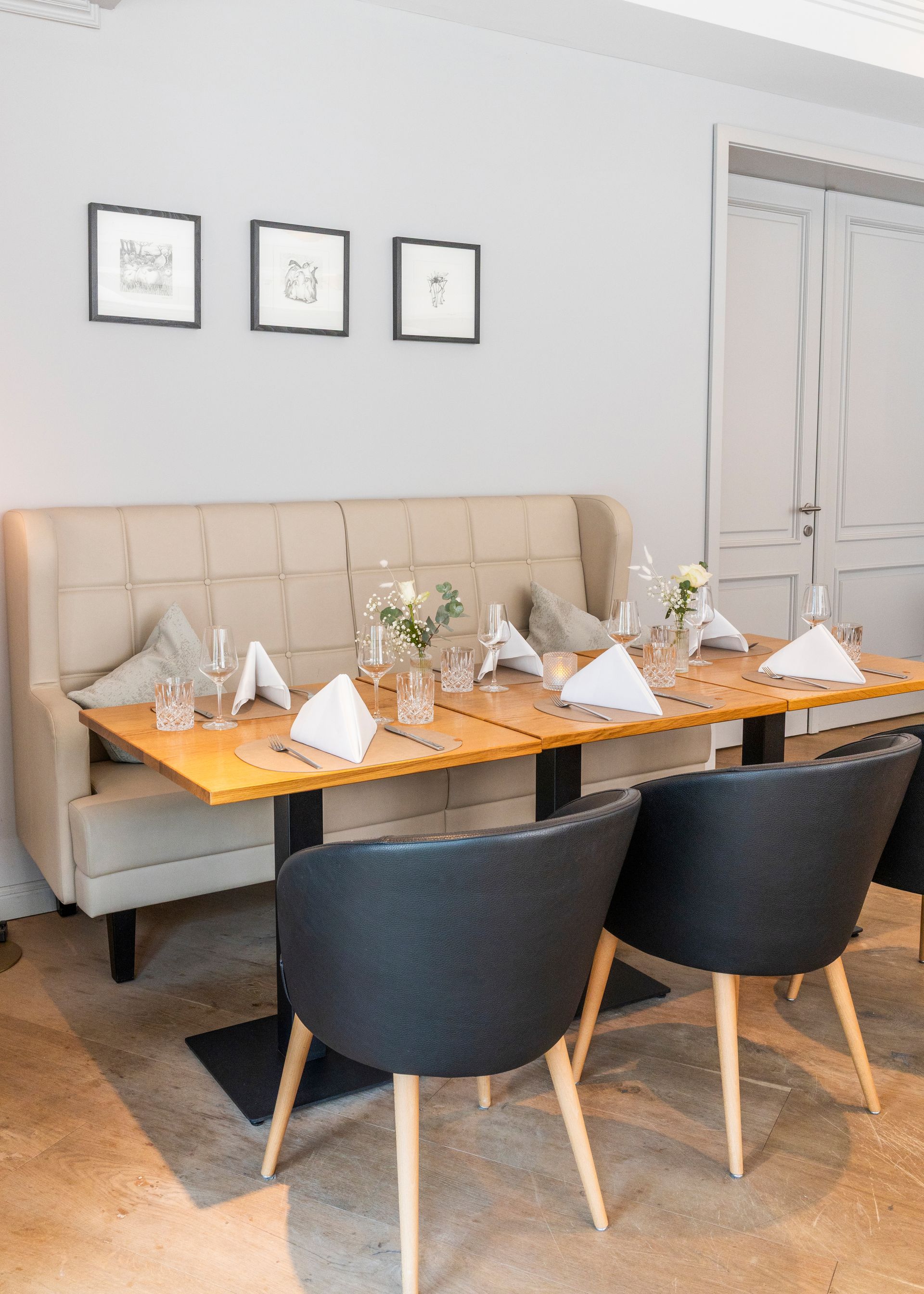 Een eethoek met een beige gestoffeerde zithoek, een houten tafel en twee donkergrijze stoelen tegen lichte muren.