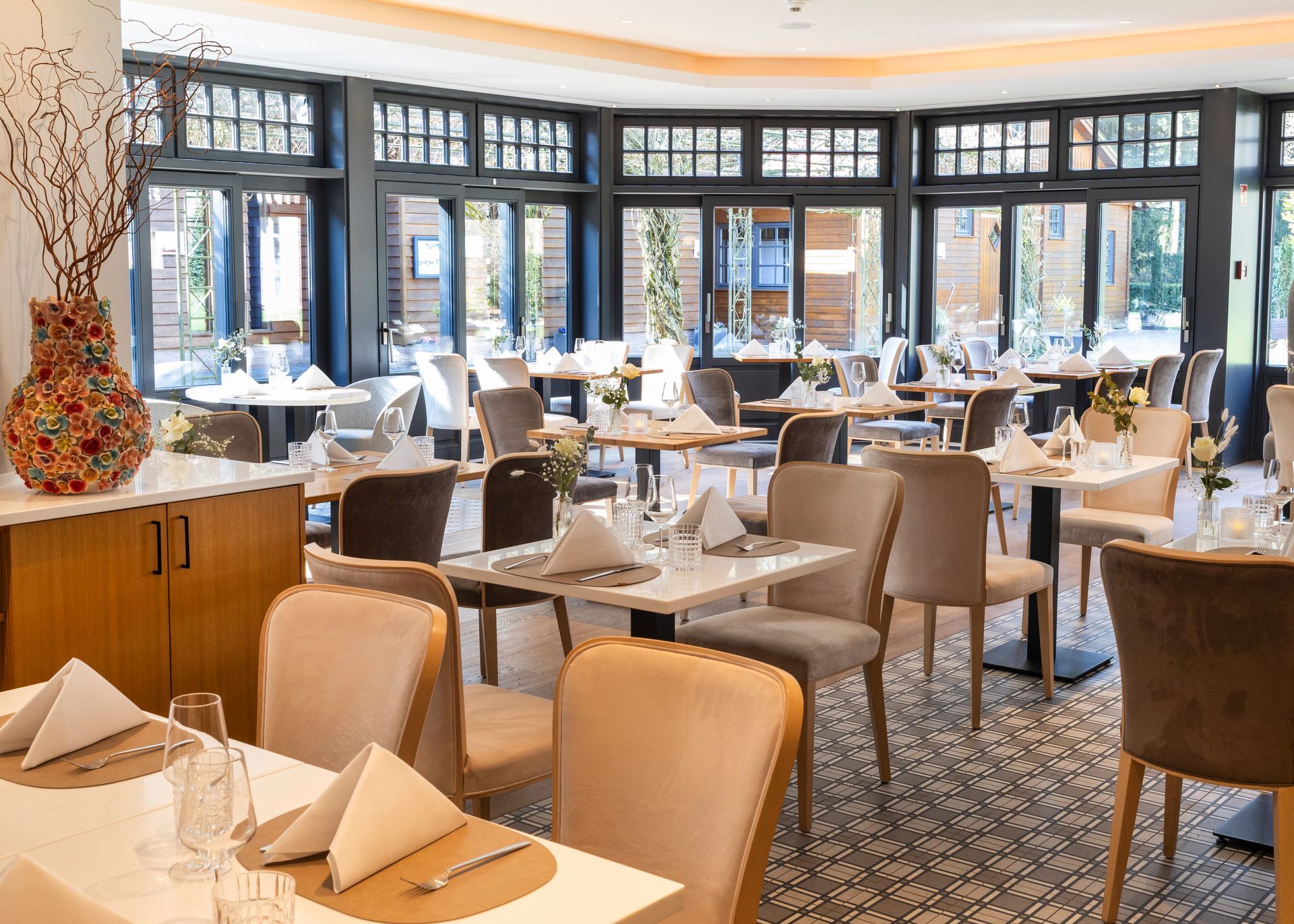 Een elegant restaurant met een eetzaal, wit gedekte tafels en stoelen, en grote ramen met uitzicht op het groen.