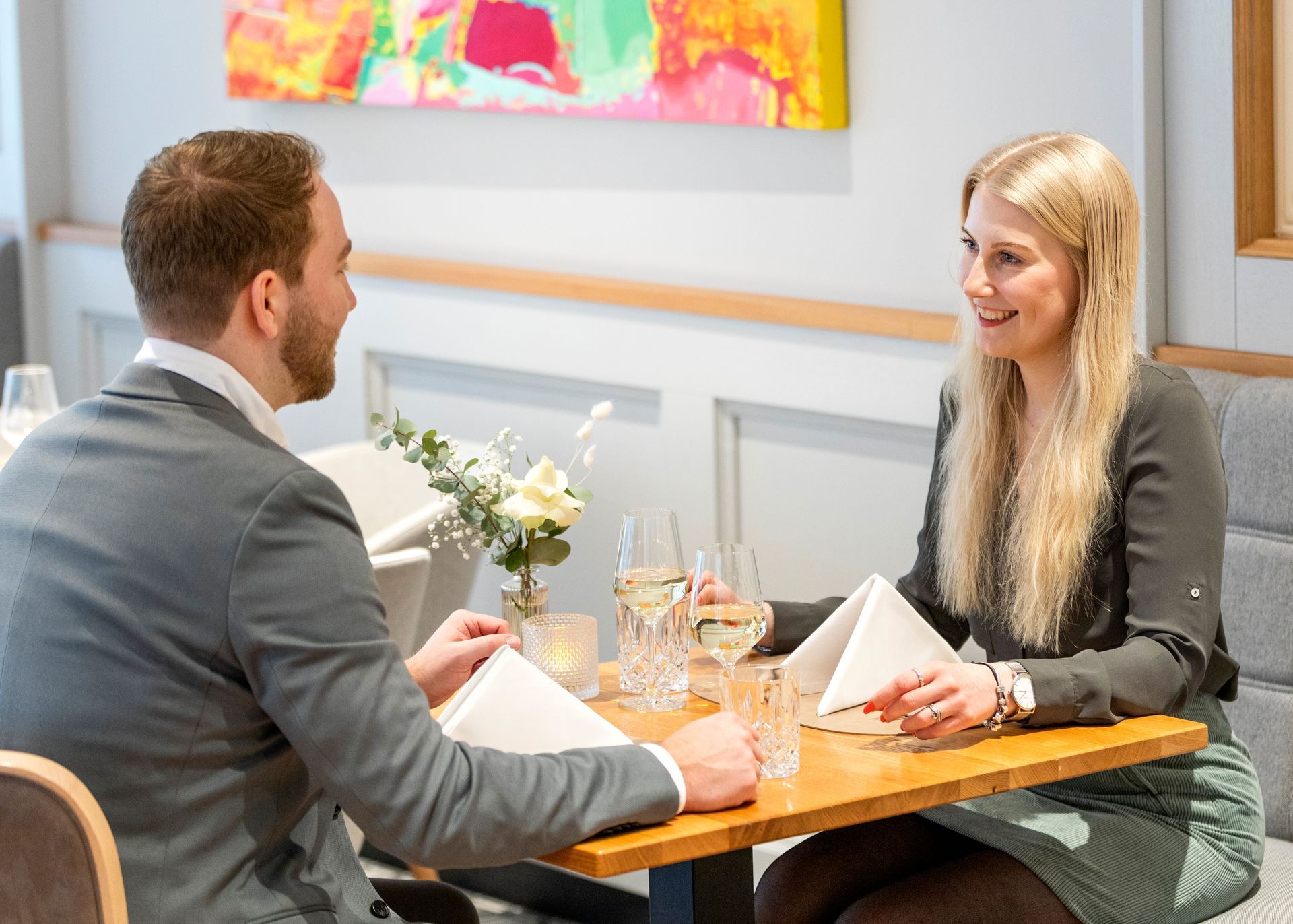 Ein Mann und eine Frau sitzen sich an einem Restauranttisch gegenüber und lächeln beim Essen in einem hell erleuchteten, modernen Raum.