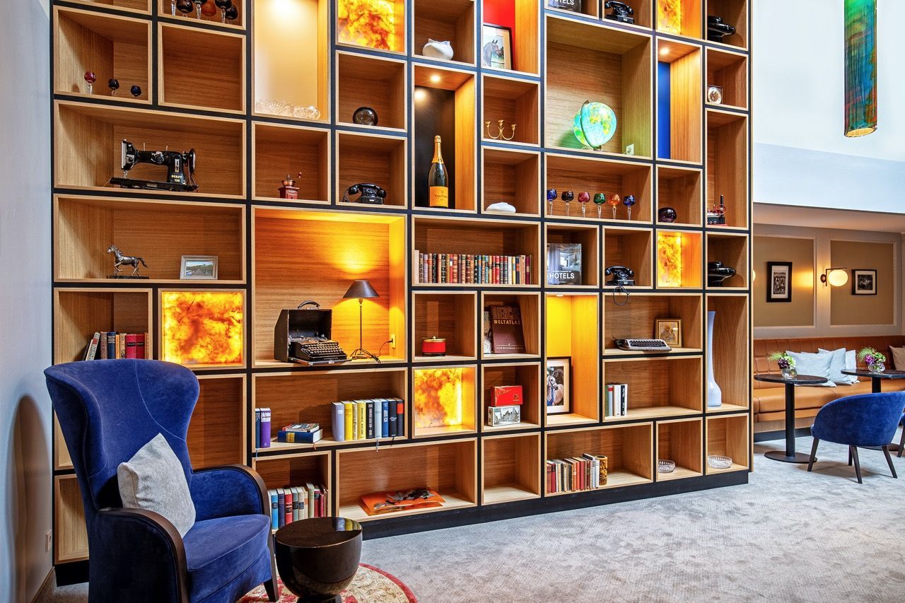 A large wooden shelving unit, filled with books and decorative items, next to a blue armchair in a modern living room.