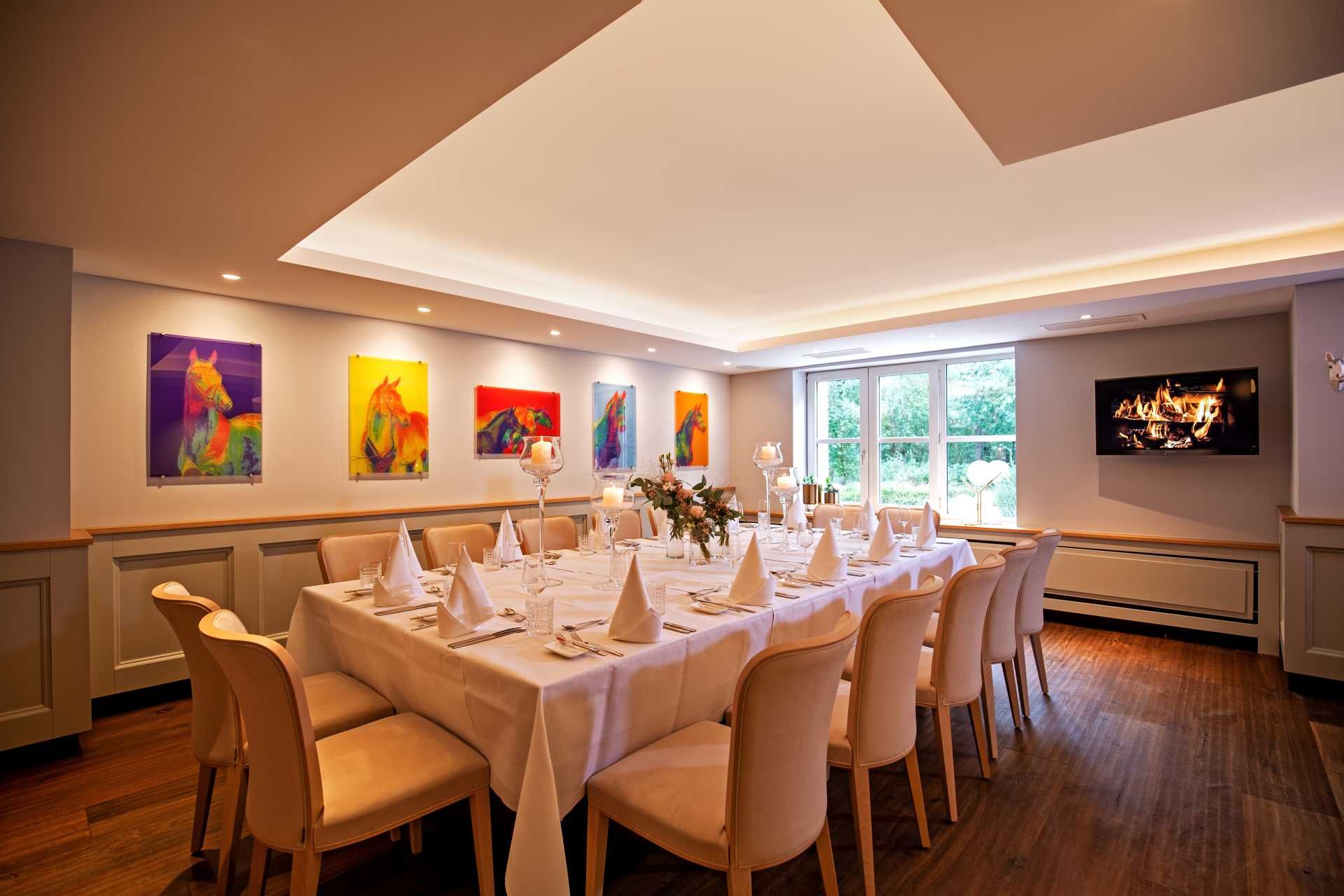 Ein formelles Esszimmer mit einer langen, für ein Bankett gedeckten Tafel, cremefarbenen Stühlen und farbenfrohen Kunstwerken an den Wänden.