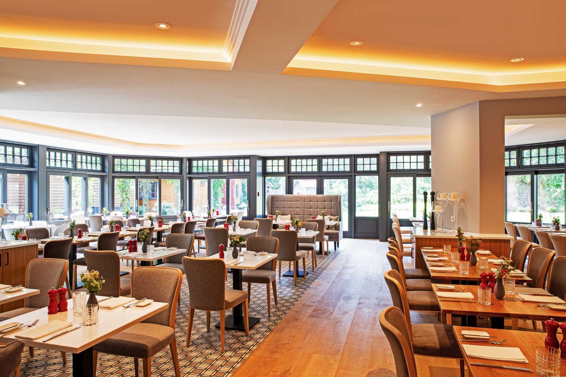 Een licht, modern restaurantinterieur met houten vloeren, eetkamerstoelen in neutrale tinten en tafels die voor de gasten zijn gedekt.