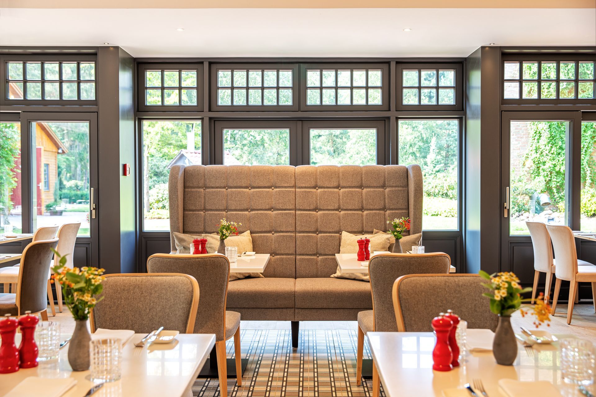 Ein gut beleuchteter Restaurantinnenraum mit gedeckten Tischen, die auf einen großen, hohen, grau gepolsterten Sitzbereich mit Nischen ausgerichtet sind.