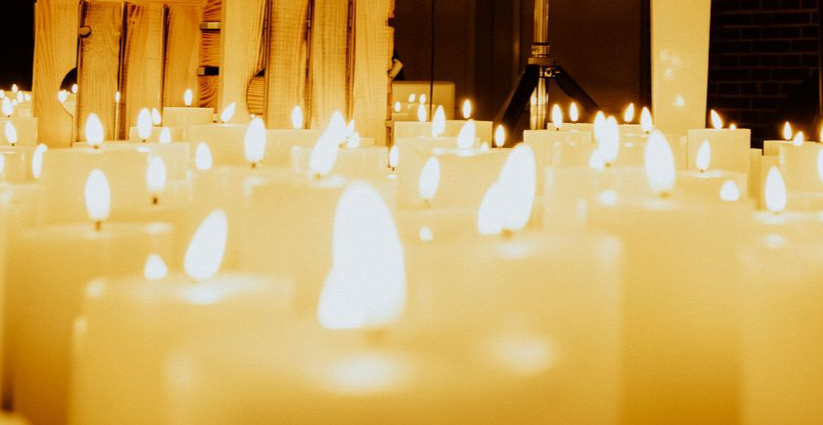 Eine dichte Ansammlung weißer Kerzen mit leuchtenden Flammen, getaucht in ein warmes, goldenes Licht.