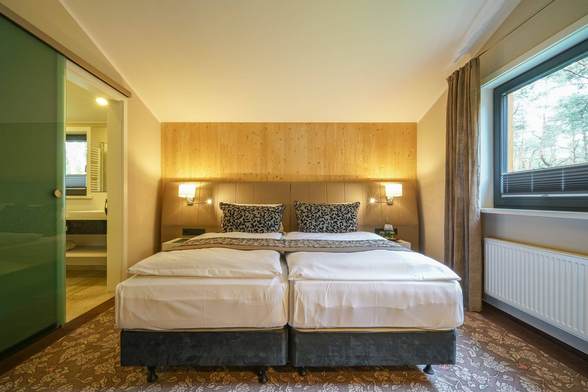 Ein modernes Hotelzimmer mit zwei Einzelbetten, einer holzgetäfelten Akzentwand, gemusterten Zierkissen und einem angrenzenden Badezimmer.