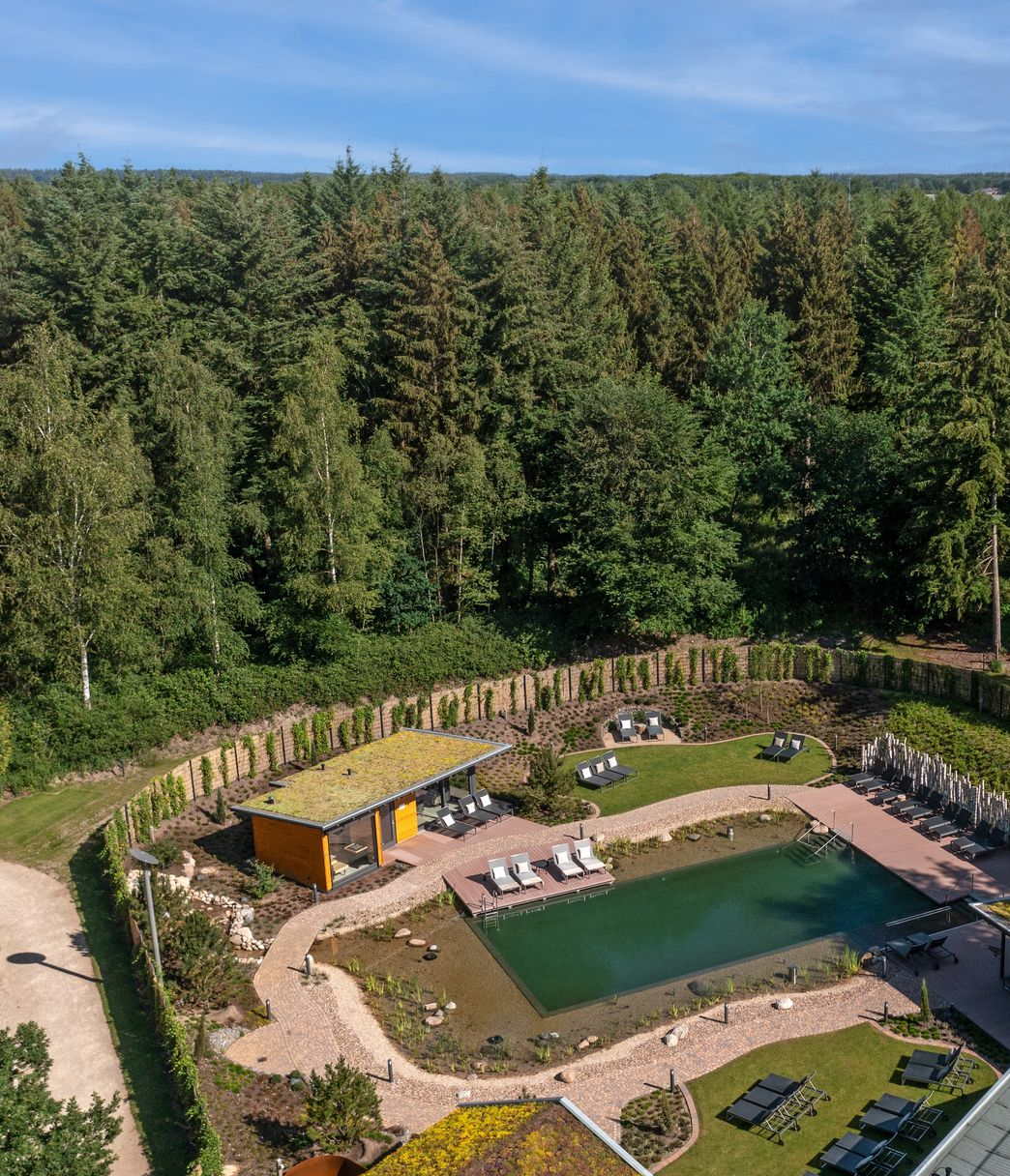 Ein natürlicher Swimmingpool und eine kleine Hütte mit Gründach, eingebettet in einen Garten neben einem dichten Wald.