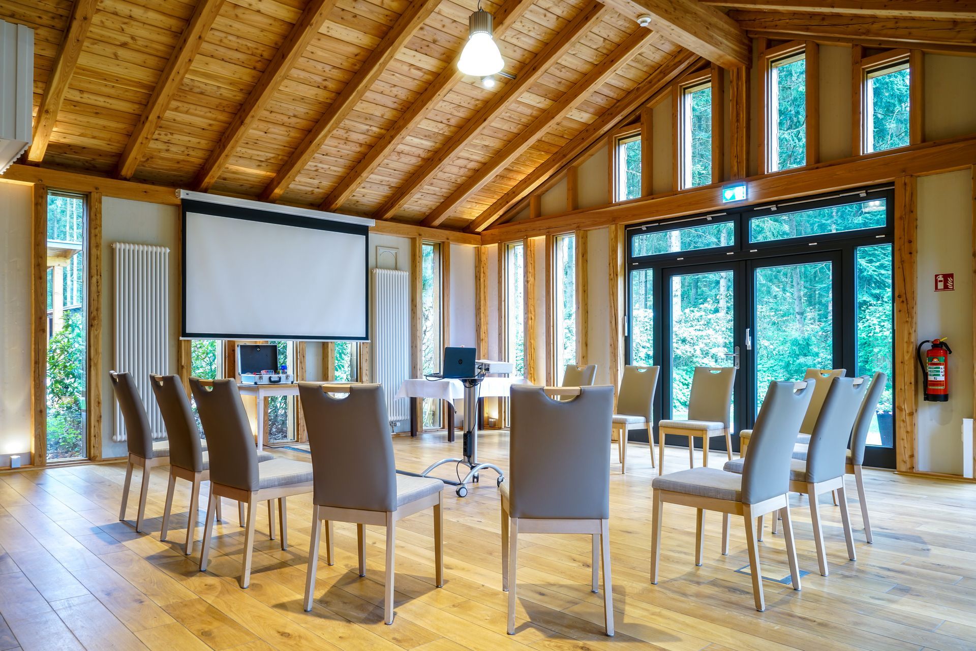 Ein Besprechungsraum mit Wänden und Decke aus Holz, in dem graue Stühle im Kreis vor einer Projektionsfläche angeordnet sind.