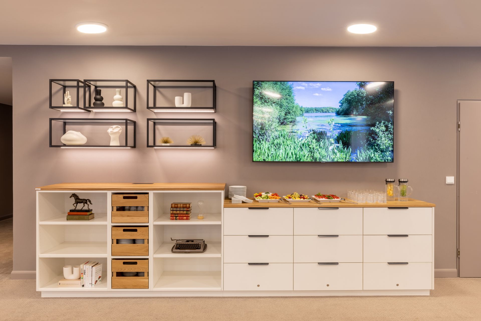 Eine moderne Wand mit Fernseher, schwebenden Metallregalen mit Dekoration und einem weißen Schrank mit Aufbewahrungsboxen aus Holz.