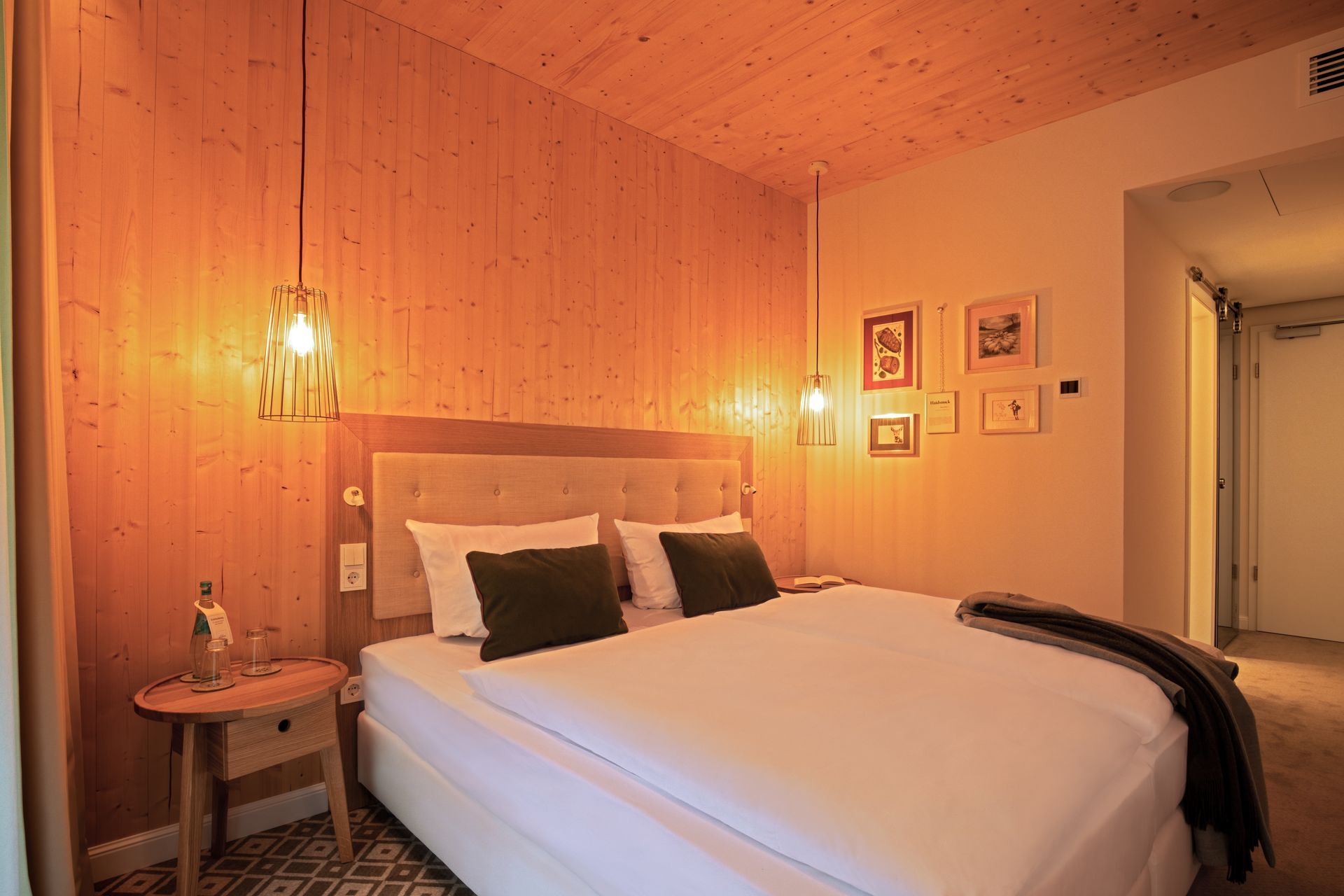 A hotel room with a neatly made bed, patterned pillows, a floral headboard, two bedside lamps, and a chair.