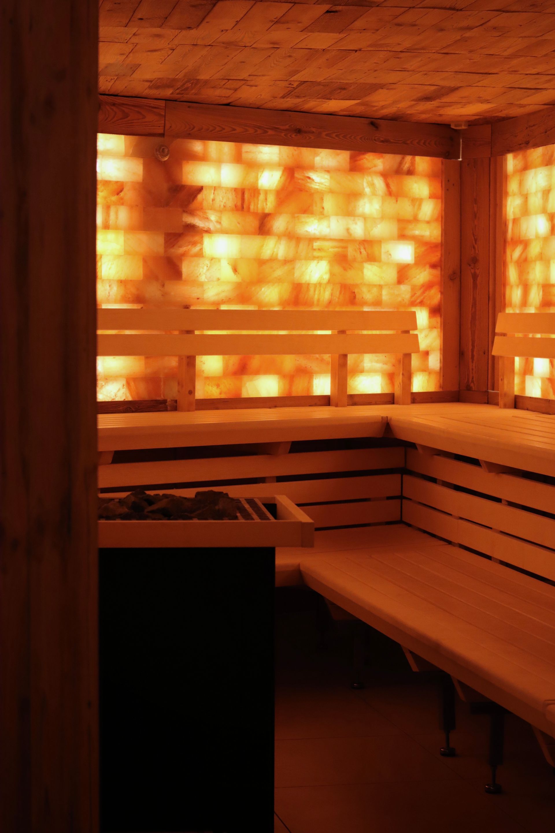 Eine Holzsauna mit Bänken und einer leuchtenden, hinterleuchteten Wand aus Himalaya-Salzziegeln.