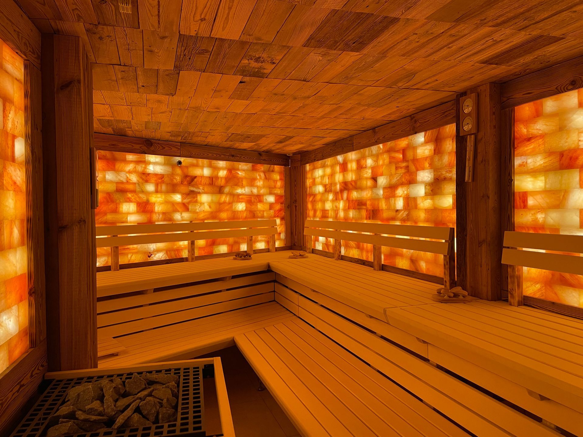 Eine Salzsauna im Innenbereich mit Wänden aus beleuchteten orangefarbenen Himalaya-Salzblöcken sowie Bänken und Decke aus Holz.