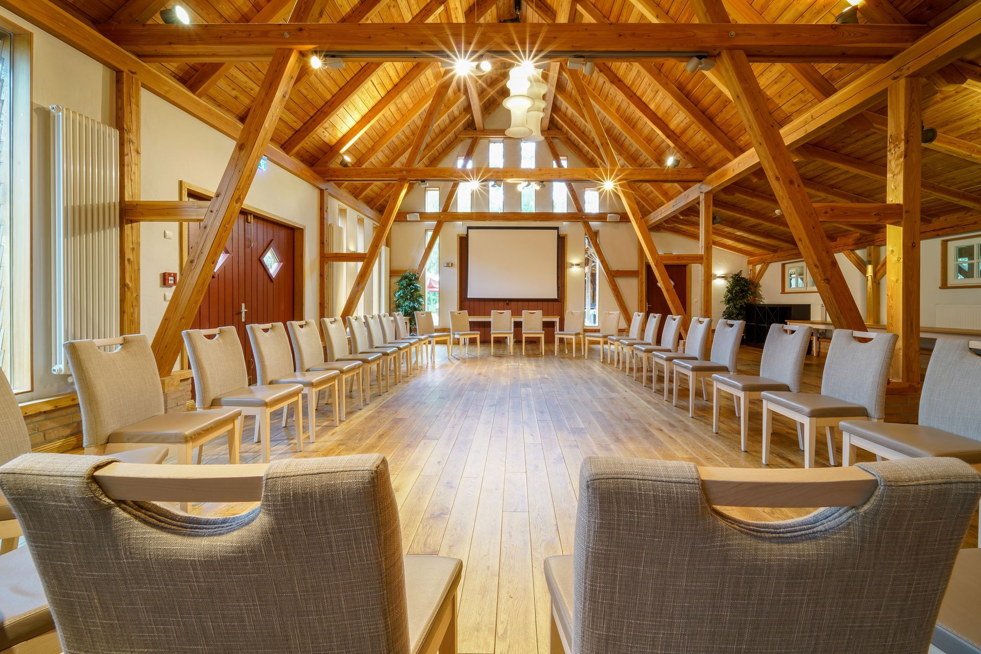 A bright, rustic conference room with exposed wood beams, a large screen, and chairs arranged in a U-shape.