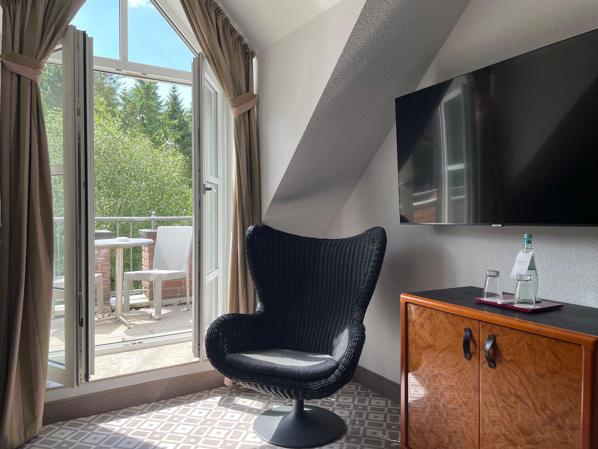 Ein modernes Hotelzimmer mit einem ordentlich gemachten Doppelbett, dunkel gemusterten Kissen, Wandlampen und einer kleinen Sitzecke.