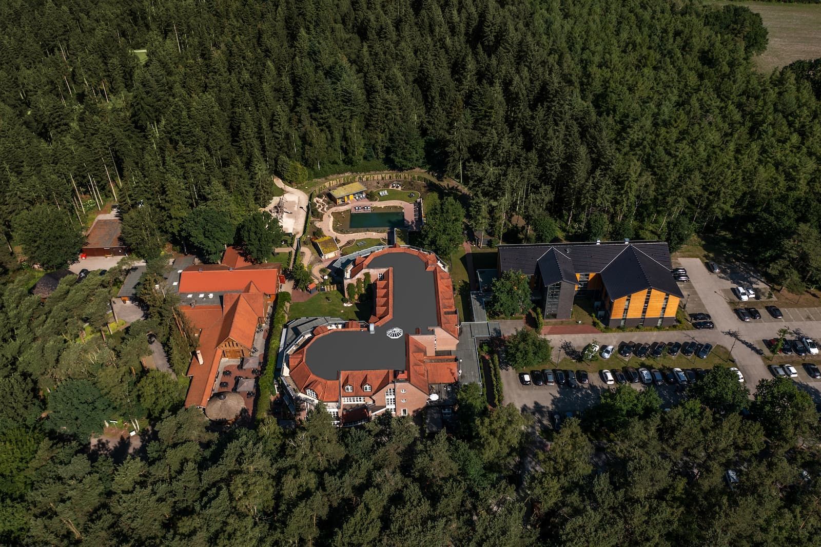 Luftaufnahme eines weitläufigen Hotelkomplexes mit Terrakotta-Dächern, umgeben von dichtem Wald, inklusive Schwimmbad.