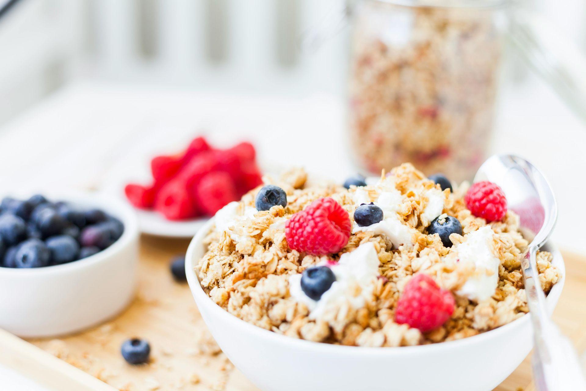 A bowl of cereal topped with fresh blueberries and raspberries, with a small bowl of berries and a glass of cereal on the side.