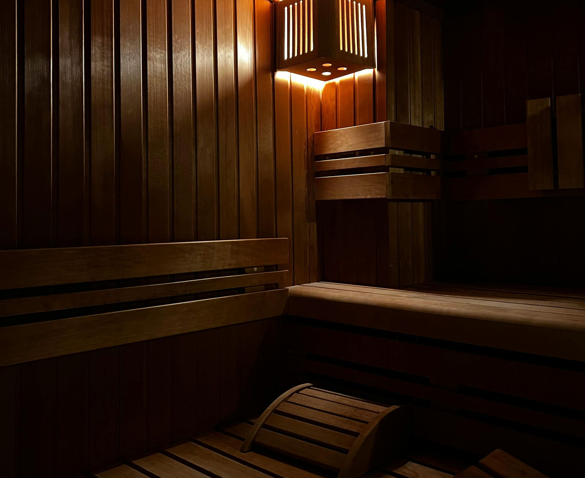 Een lege saunaruimte met warm, gedempt licht, houten lambrisering en houten banken.