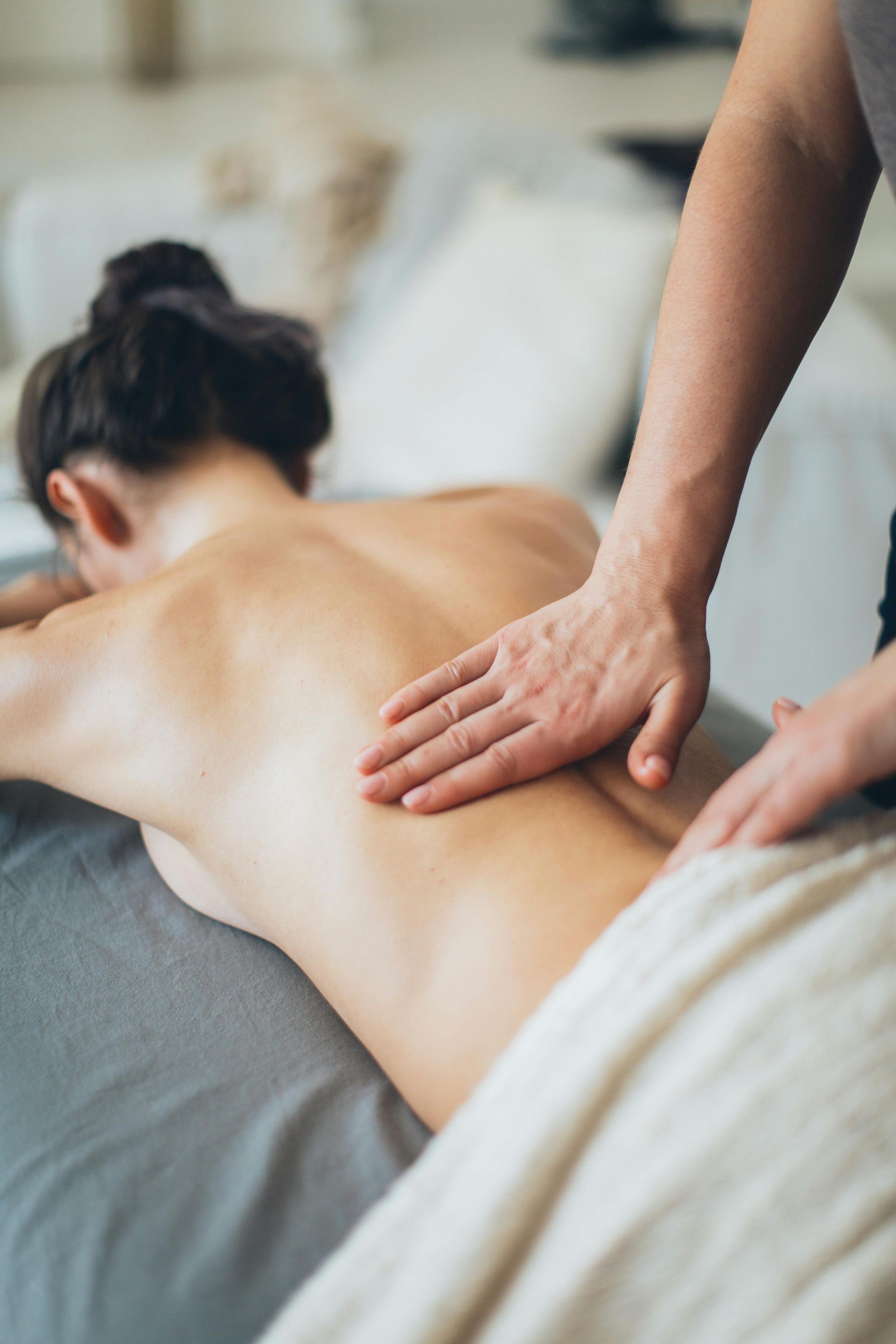 A professional massage therapist is massaging the back of a person lying on a massage table.