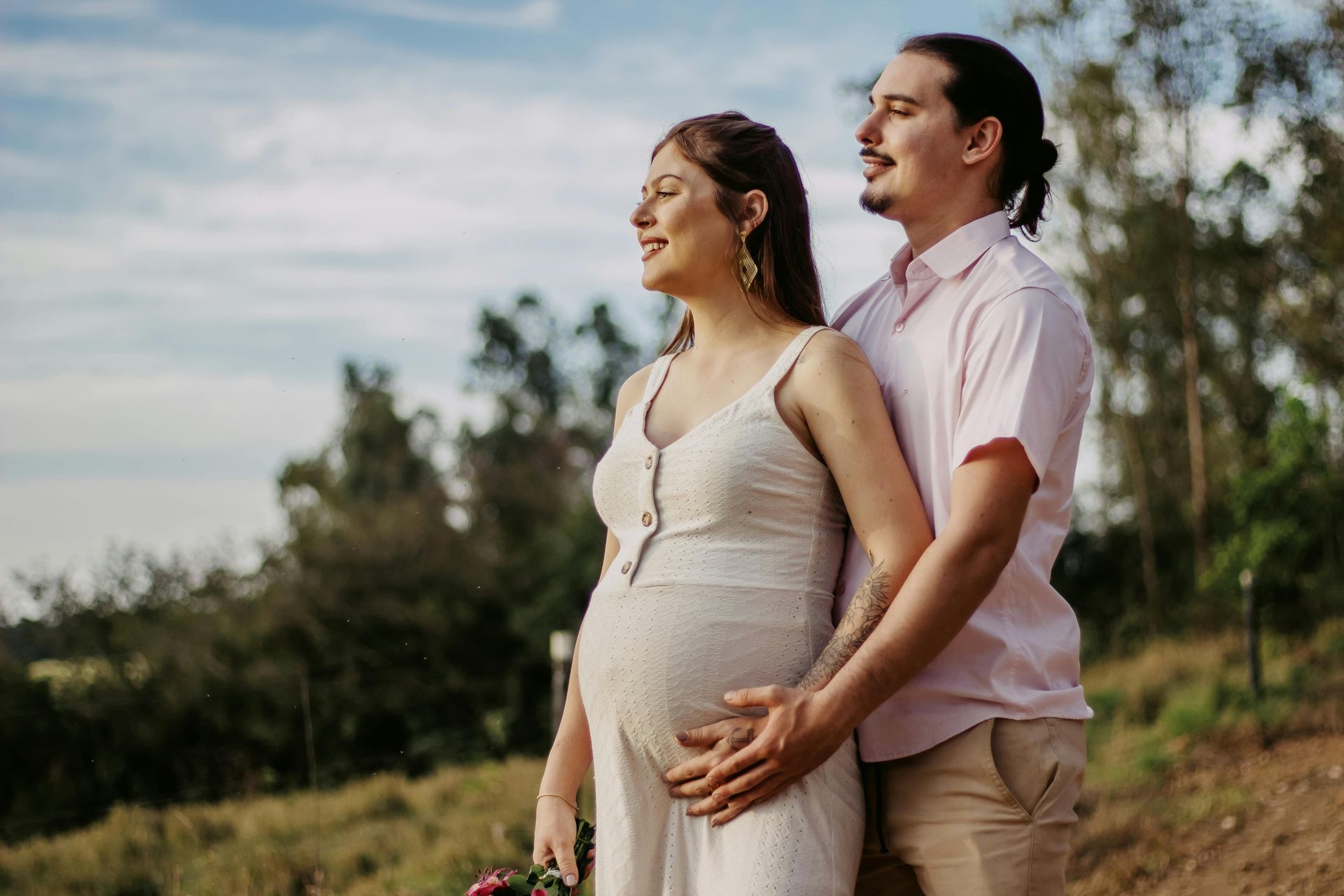 A pregnant woman and her partner are standing in a field, looking toward the horizon.