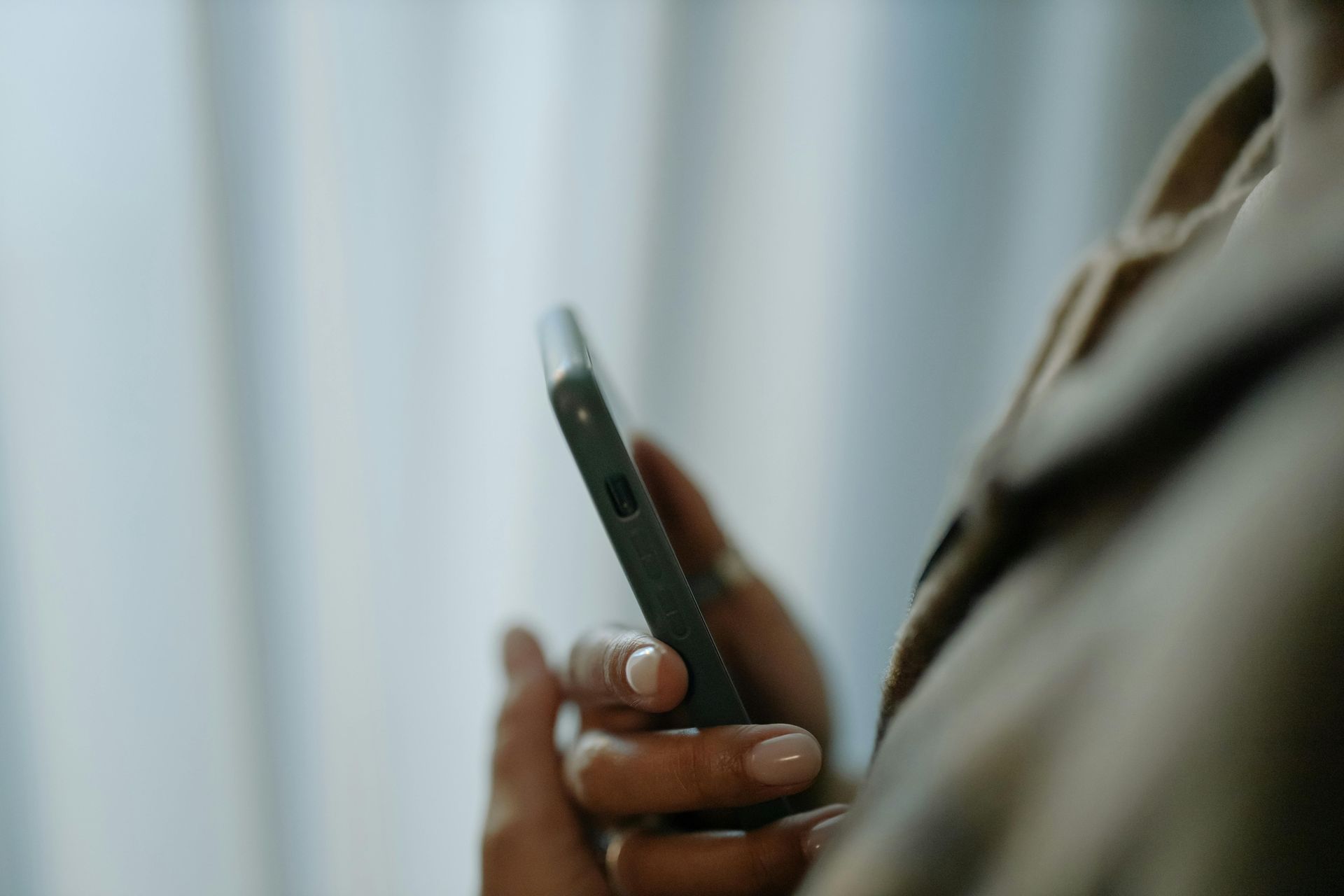 Close-up of hands holding a dark smartphone against a soft, light background.