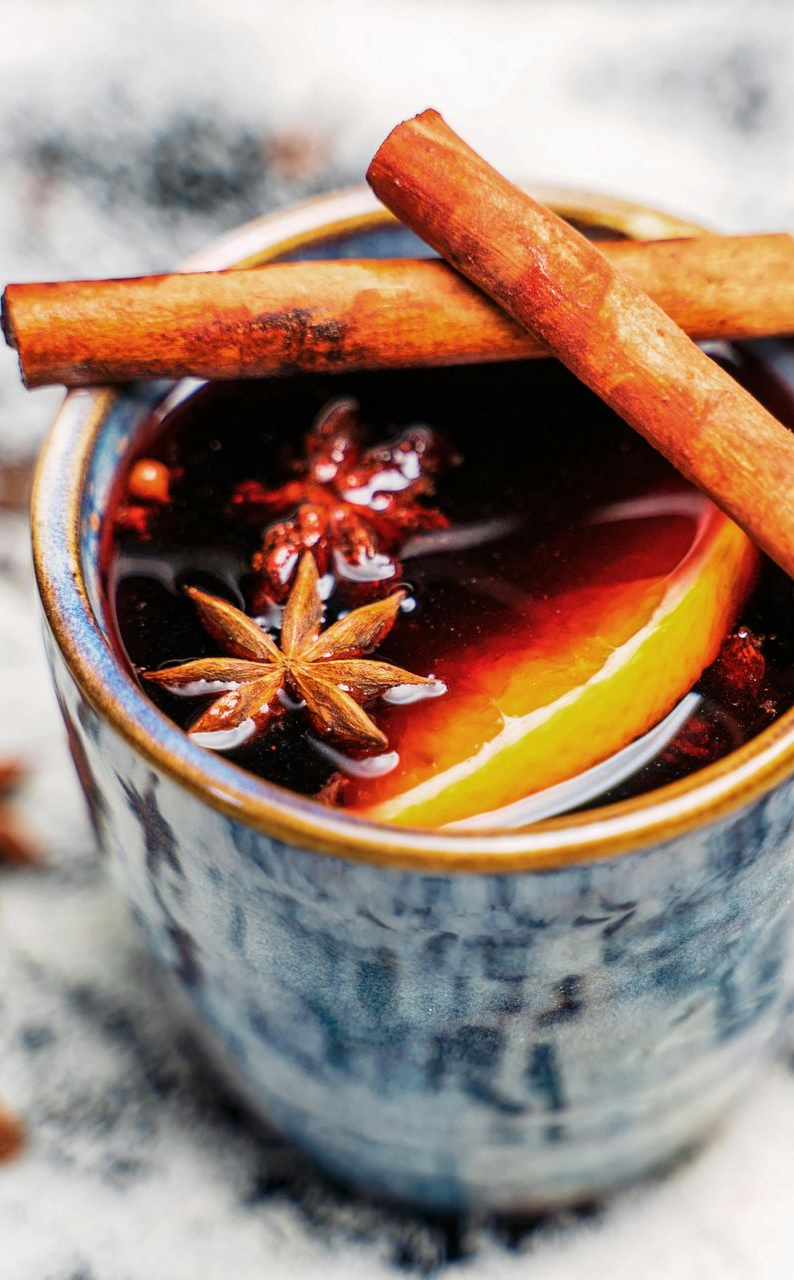 A rustic mug filled with mulled wine, garnished with a cinnamon stick, star anise, and a slice of orange.