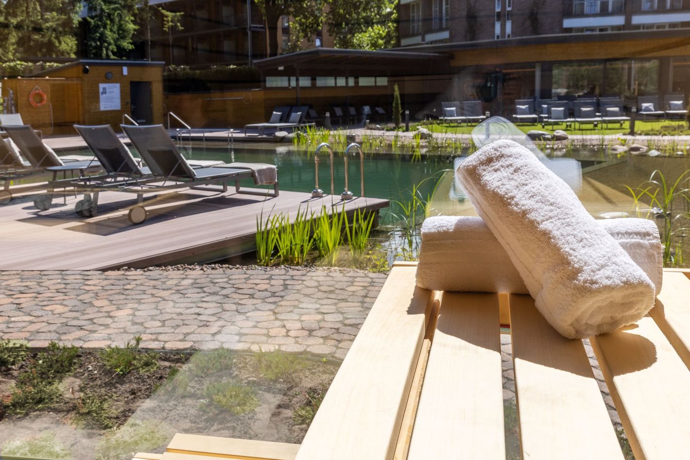 Eine Reihe grauer Liegestühle in einem modernen, sonnendurchfluteten Ruheraum mit großen Fenstern und Blick auf einen Garten.