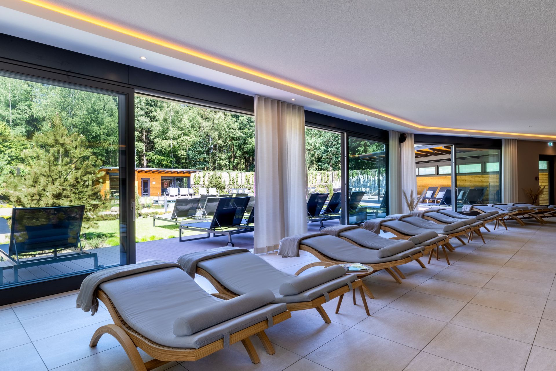 Een moderne, lichte zitkamer met rijen grijze fauteuils die uitkijken op grote ramen met uitzicht op een tuin.