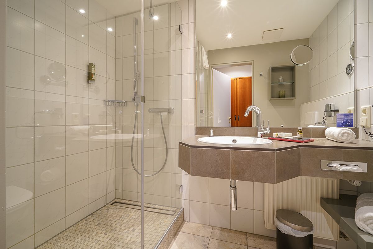 Ein Hotelzimmer mit zwei Betten, einer gemusterten Akzentwand, einem dunklen Kopfteil, grünen und magentafarbenen Kissen und gerahmten Kunstwerken.