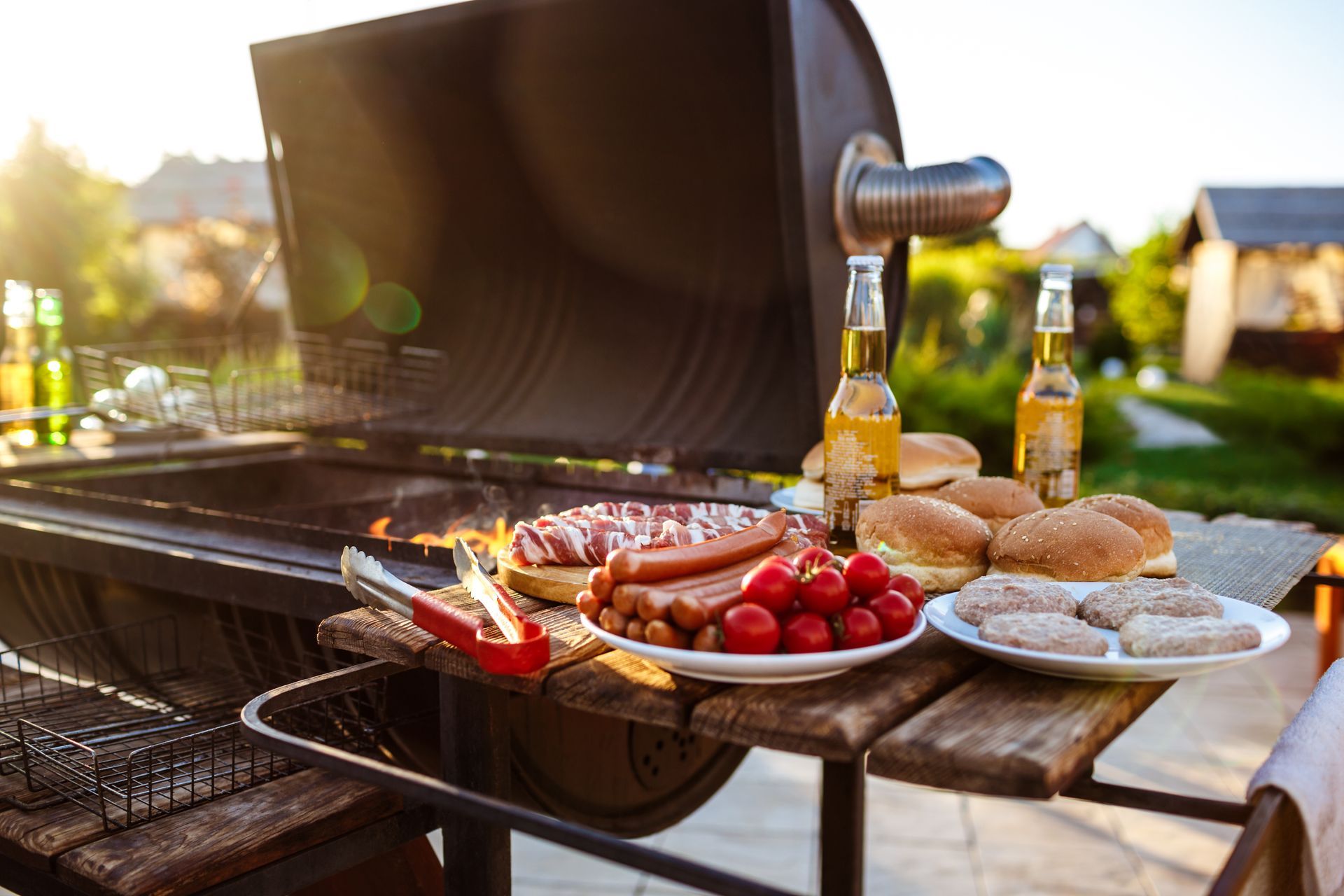 Barbecue en plein air avec saucisses, pain, tomates cerises et bouteilles sur une table de patio au coucher du soleil