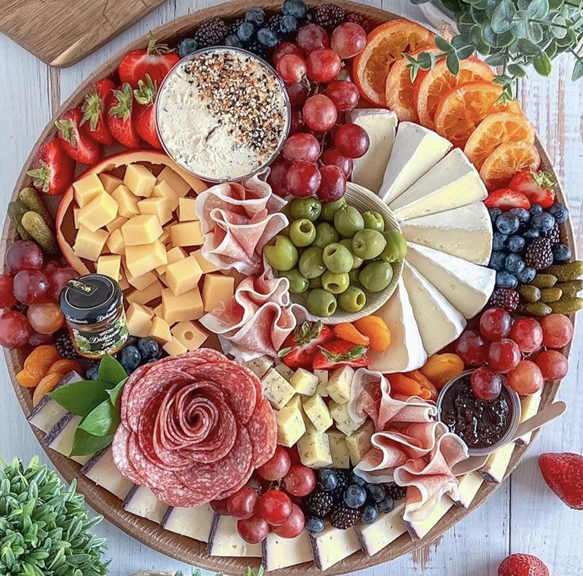 Planche de charcuterie avec fromages, raisins, baies, charcuterie tranchée, crackers et herbes aromatiques disposés en cercle