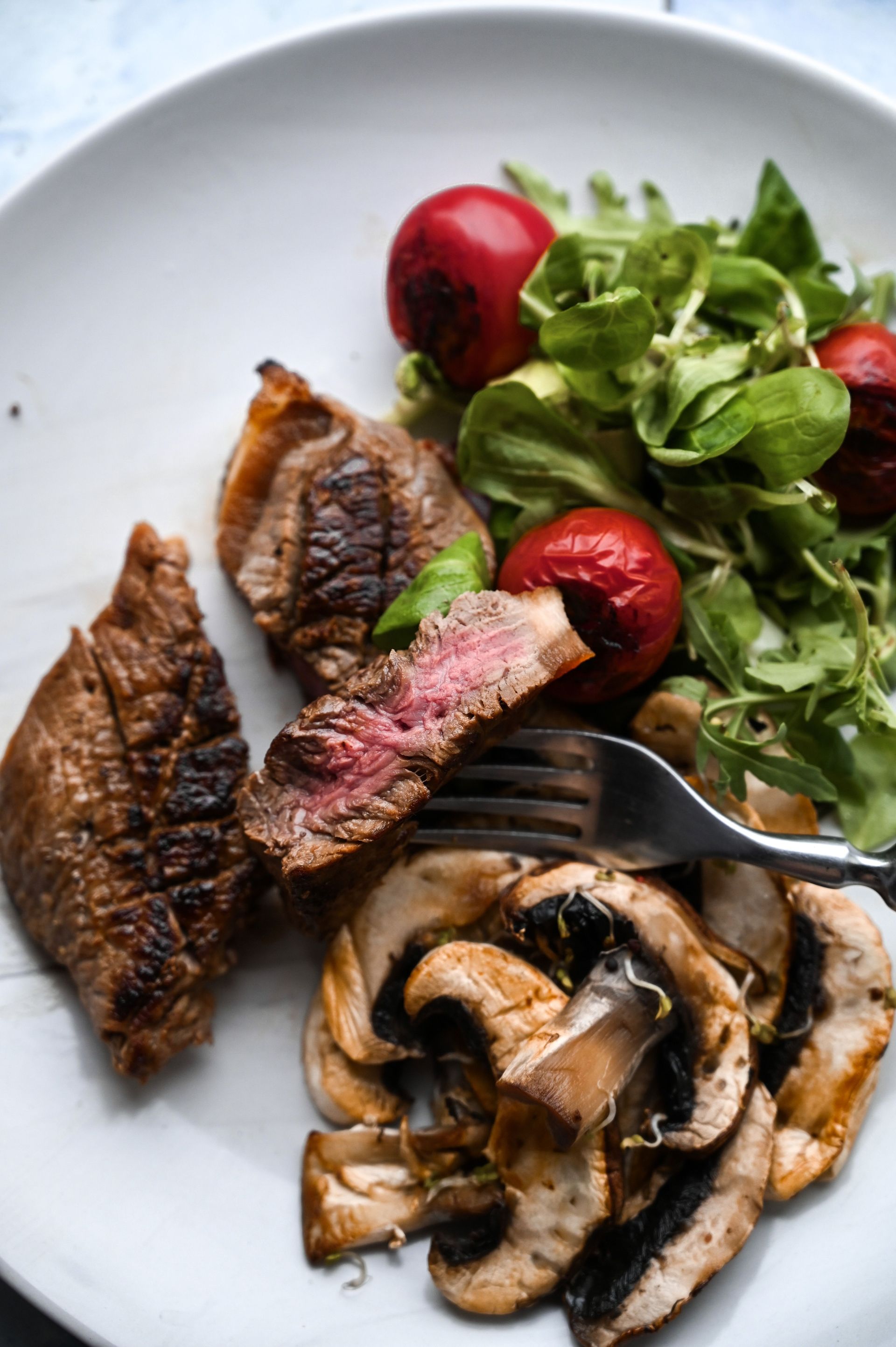 Steak grillé, champignons et salade composée avec des fraises sur une assiette blanche