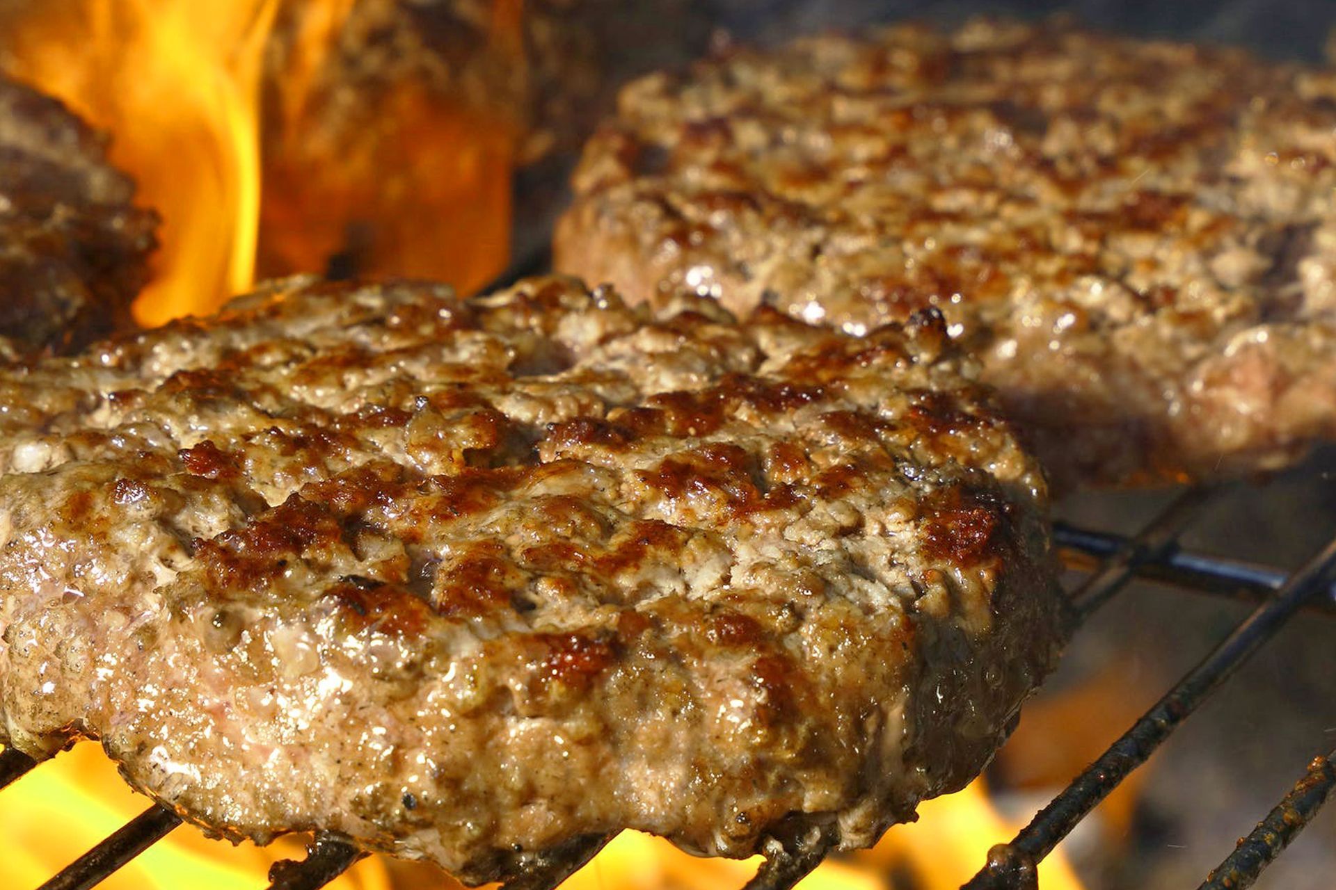 Deux hamburgers qui grillent sur un barbecue à flamme nue.