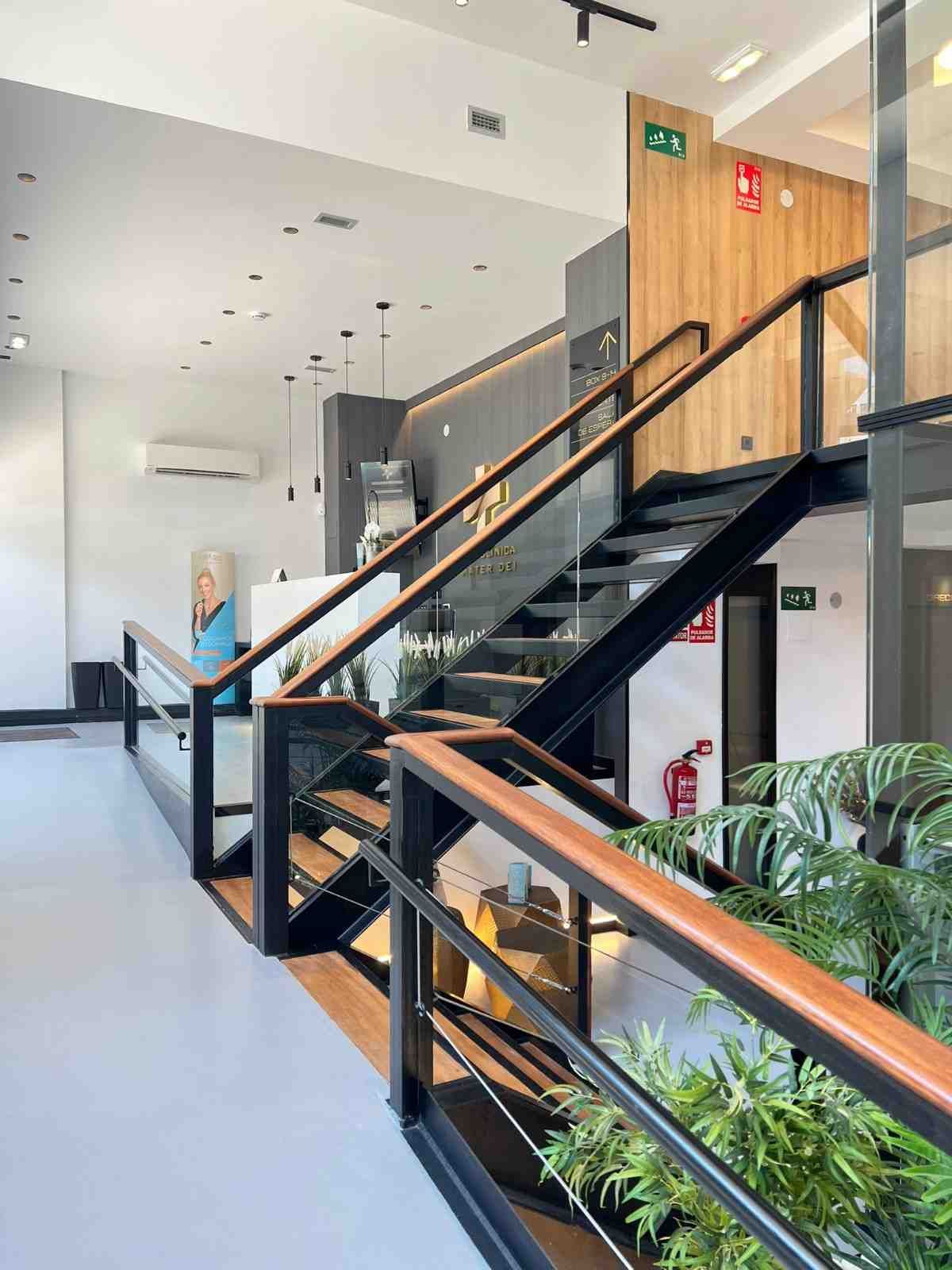 Interior moderno con una escalera de metal negro con pasamanos de madera, una mampara de cristal