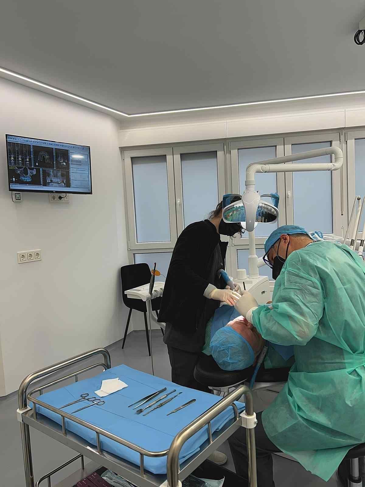 Unas manos enguantadas, sobre un fondo azul claro, sostienen un pequeño modelo de diente azul y un espejo dental.