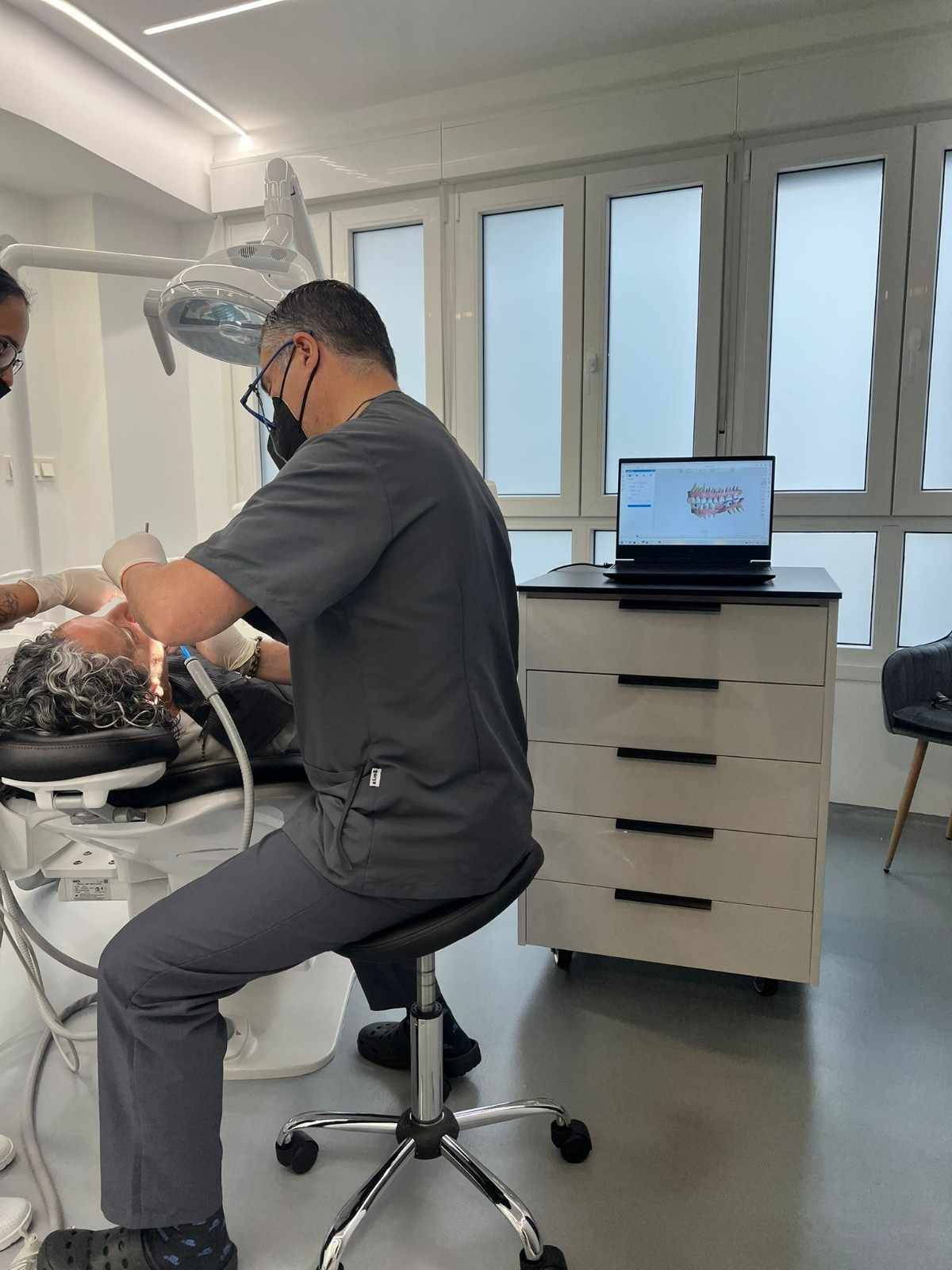 Dentista con bata blanca y guantes, sosteniendo un explorador dental y un modelo de dientes.