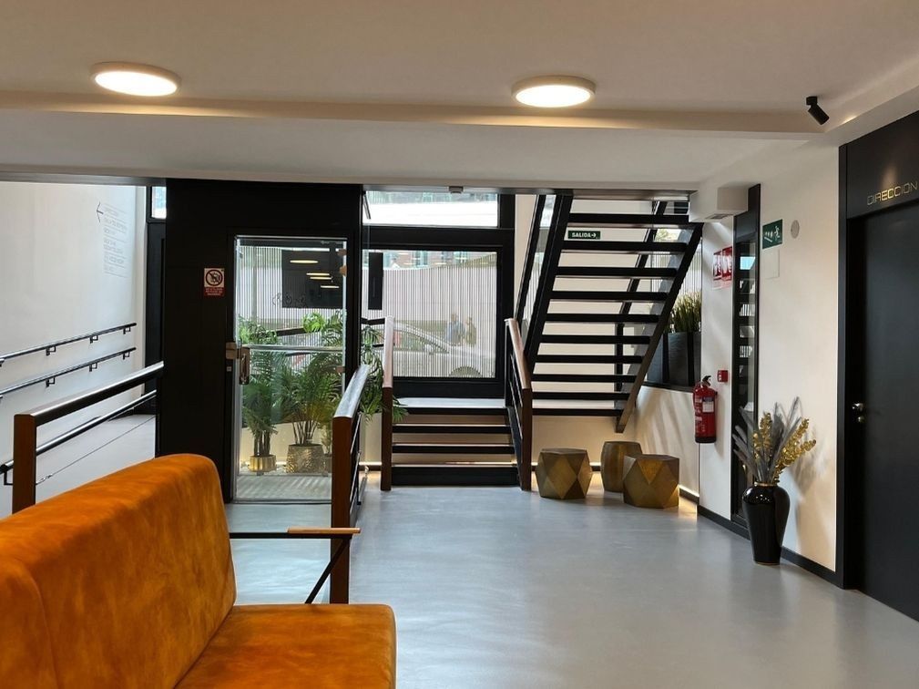 Un vestíbulo luminoso y moderno con un sofá naranja, una escalera de metal negro, una puerta de cristal