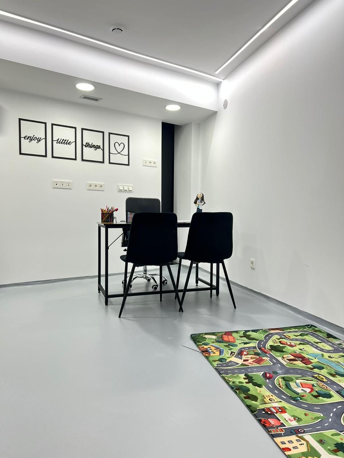 Una oficina minimalista con dos sillas negras en un escritorio, una alfombra de juegos infantil en el suelo