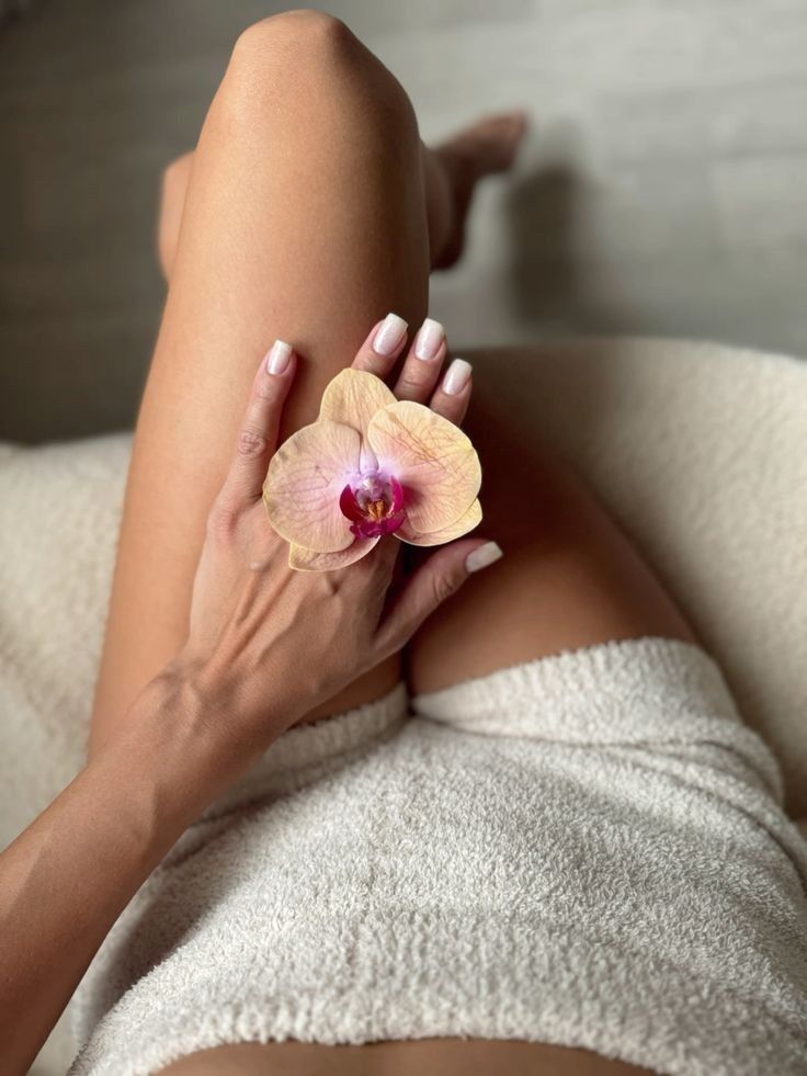 Una mano con uñas de color rosa pálido descansa sobre un regazo, sosteniendo una delicada flor