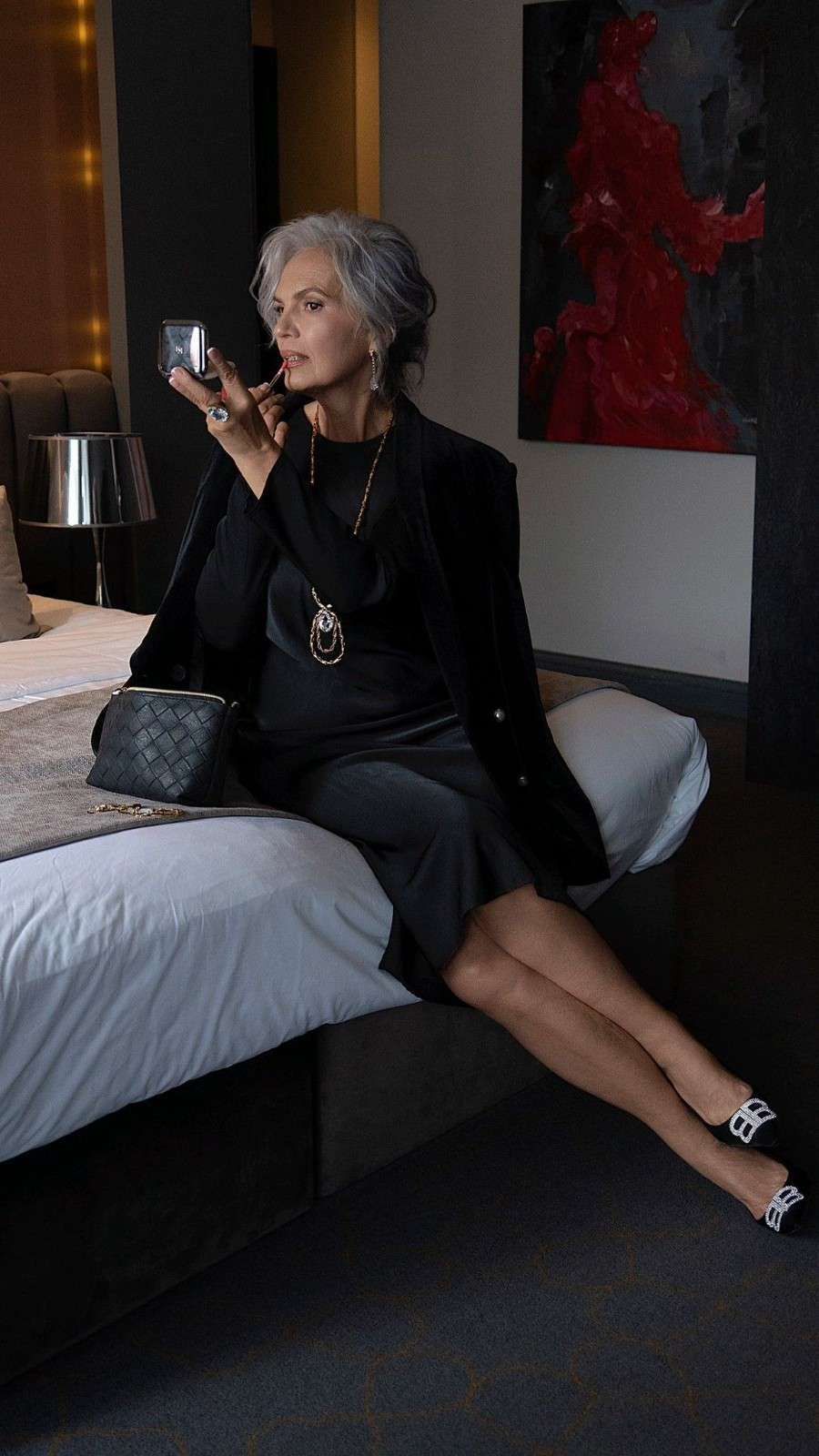 Una persona con el pelo corto y gris y una blusa blanca que le toca el cuello y el pelo, sobre un fondo gris liso.