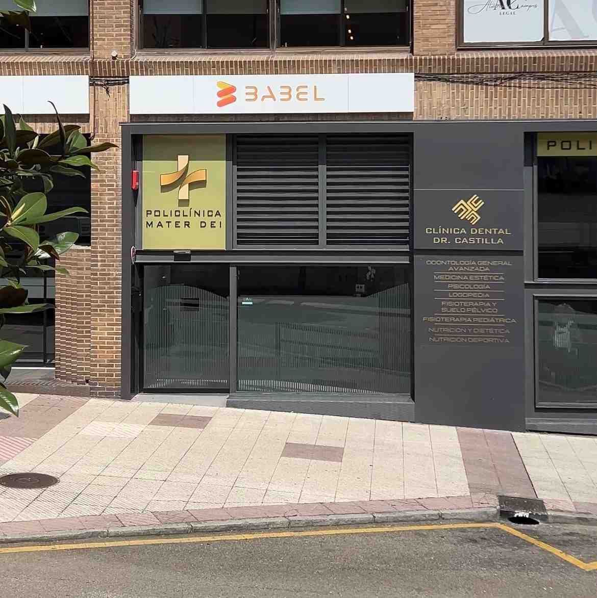 Vista a pie de calle de una tienda con fachada gris, un letrero con el logotipo de una cruz médica en la ventana.