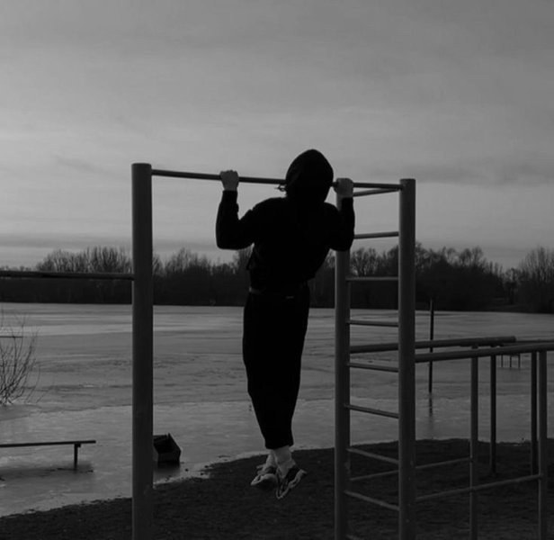 Una persona con una sudadera con capucha haciendo dominadas en una barra al aire libre, con el cielo del atardecer 