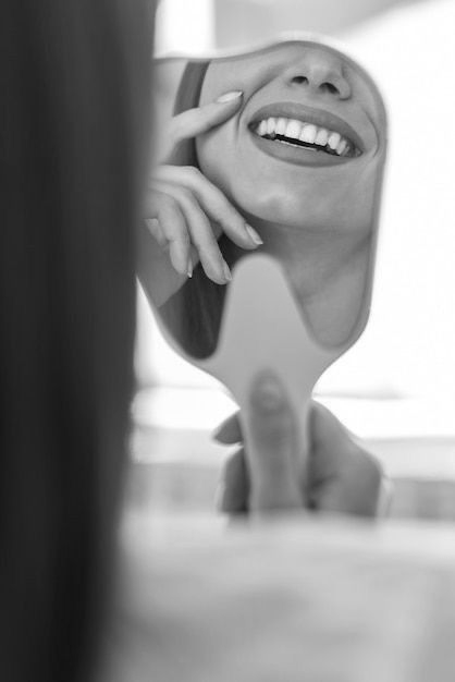 Una persona sosteniendo un espejo de mano, admirando su sonrisa y sus dientes blancos y rectos.