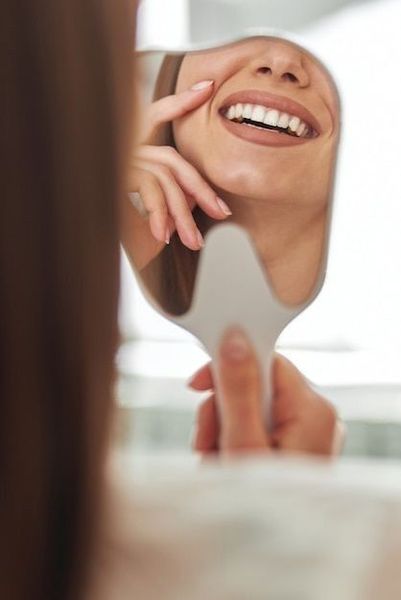 Una persona sosteniendo un espejo de mano, admirando su sonrisa y sus dientes blancos y rectos.