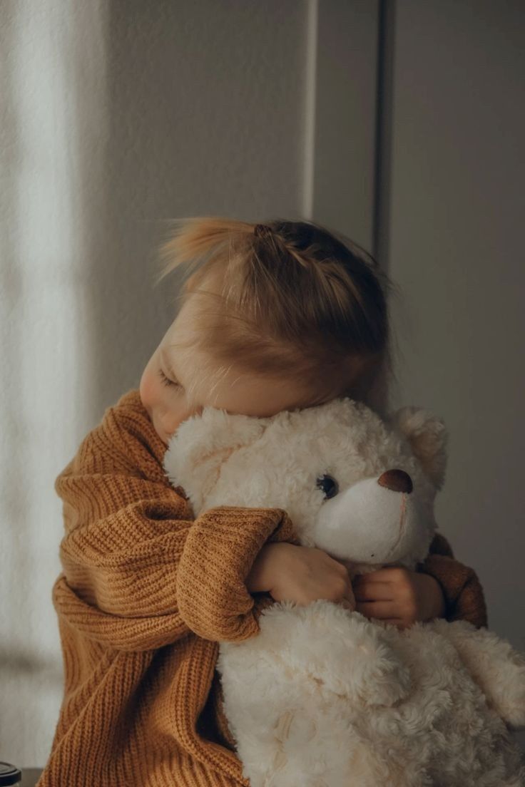 Una persona con un suéter amarillo mostaza apoya la cabeza contra un gran oso de peluche color crema al que está abrazando.
