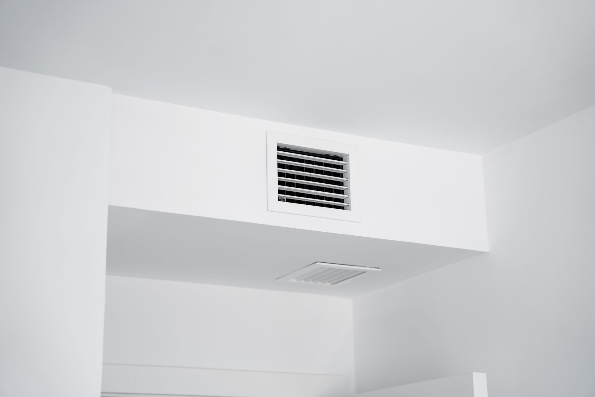 Une grille d'aération carrée blanche fixée sur le côté d'un soffite de plafond rectangulaire blanc.