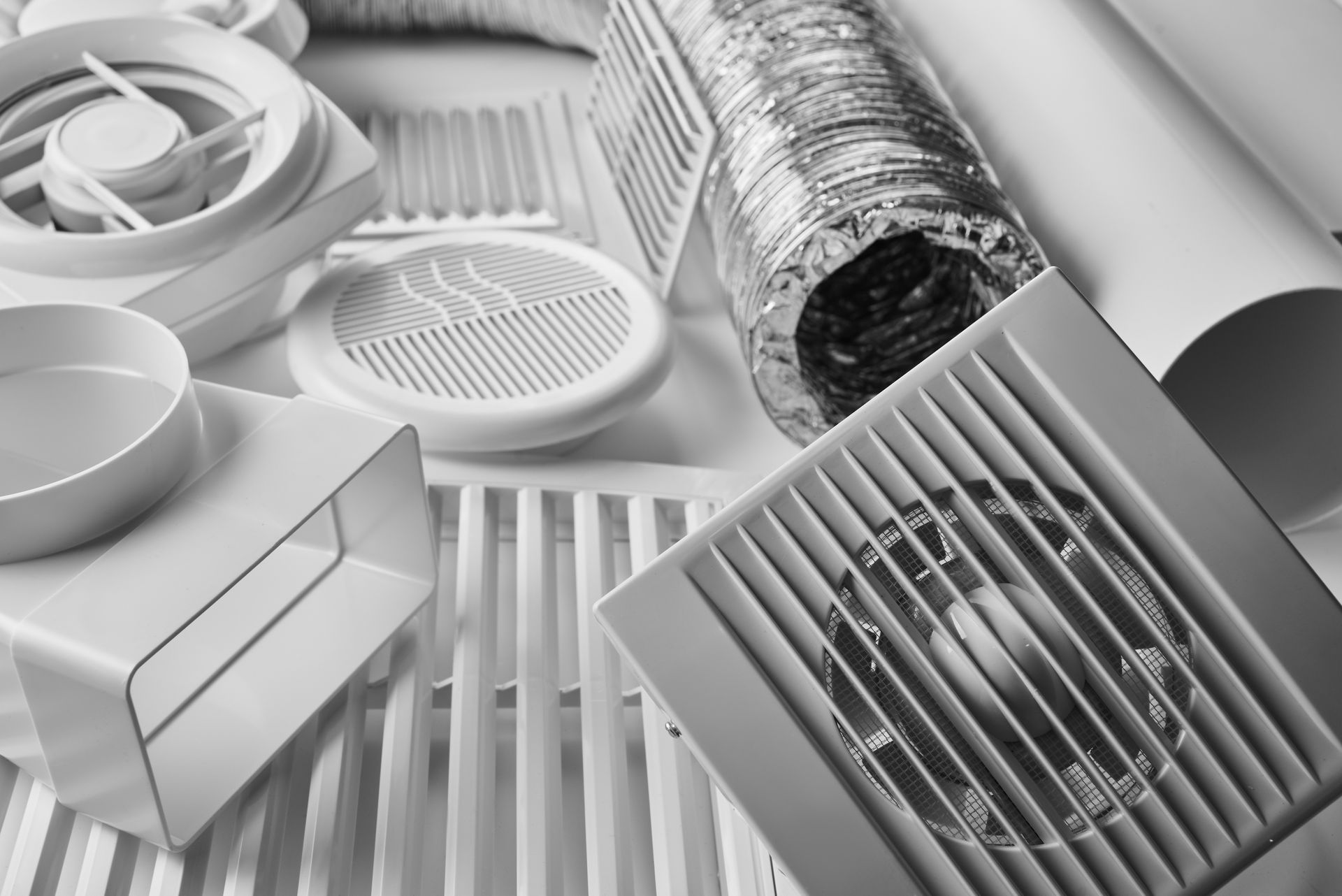 Un ensemble de grilles de ventilation et d'aérations en plastique blanc de différentes couleurs, ainsi qu'un conduit d'air flexible en métal argenté.