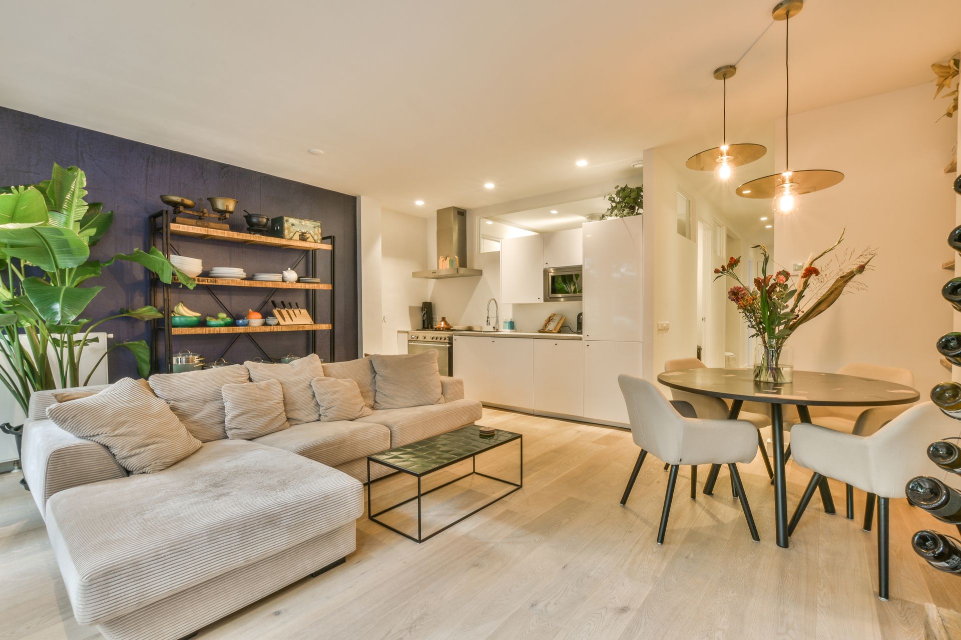 Un salon moderne et lumineux, de type open space, avec un canapé d'angle beige, une petite table basse et un coin repas.