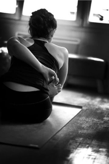Une personne assise sur un tapis de yoga dans une pièce faiblement éclairée, s'étirant avec un bras derrière le dos.